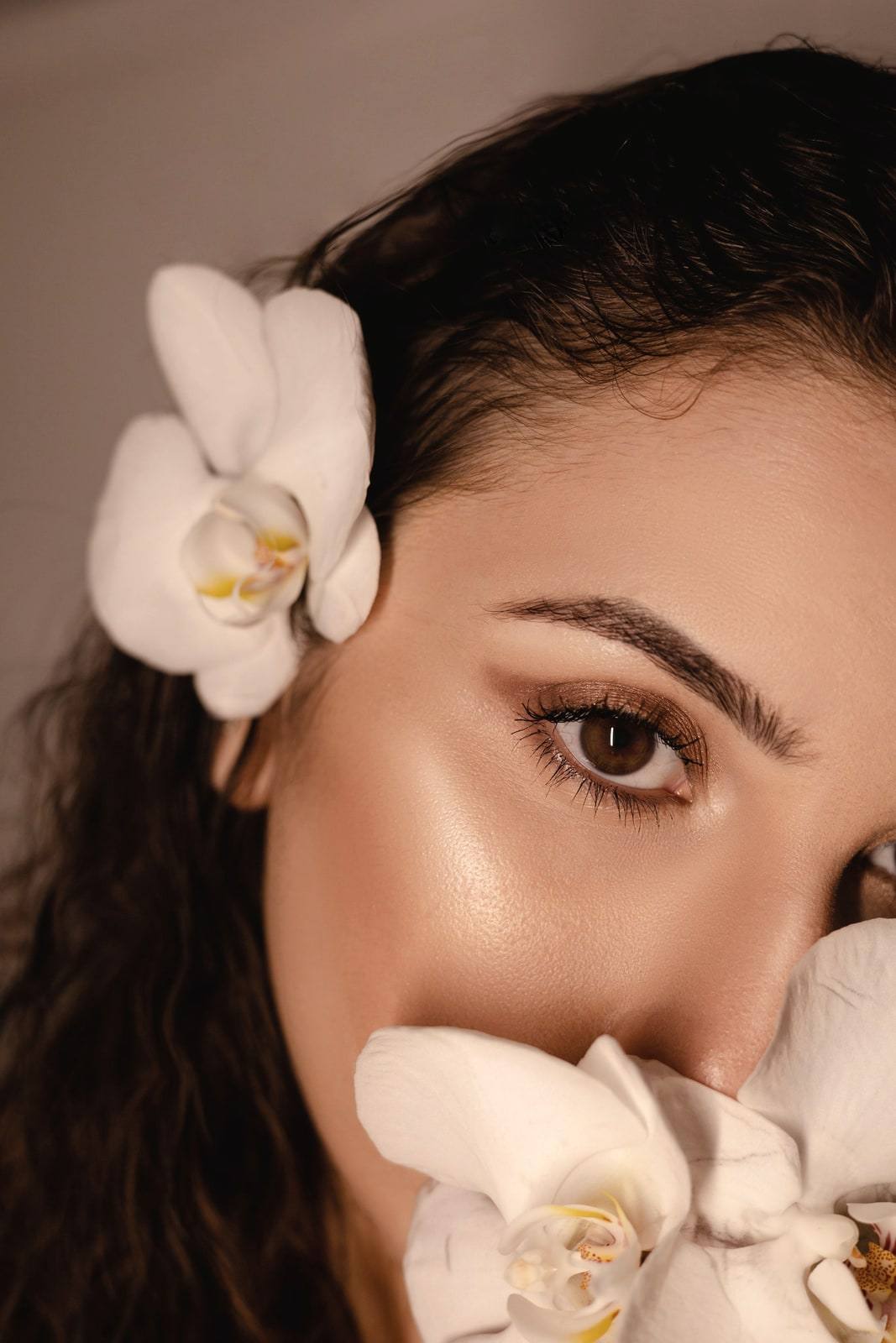 A close portrait of a woman with glowing skin and a white orchid in her hair